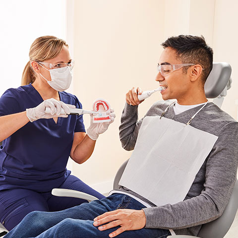 Dental Professional showing a male patient how to use electric toothbrush.